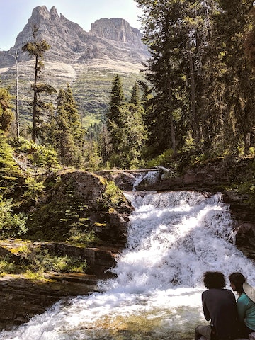 A couple sits by No Name Falls in Glacier National Park