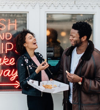 Mixed race couple on a day out at seaside having fun and laughing outside a fish and chip shop