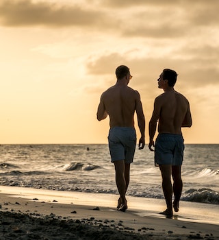 Young homosexual couple walking on the beach of Varadero during sunset, having a drink, talking and having fun together, Cuba.