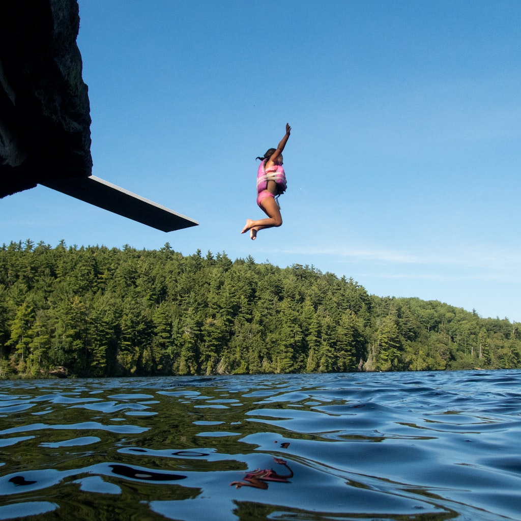 Small girl with a life jacket on, jumps off a diving board into a remote lake in Michigan's Upper Peninsula while  her brother watches.
1177965797
A small girl with a life jacket on jumps off a diving board into a remote lake in Michigan's Upper Peninsula while her brother watches.
