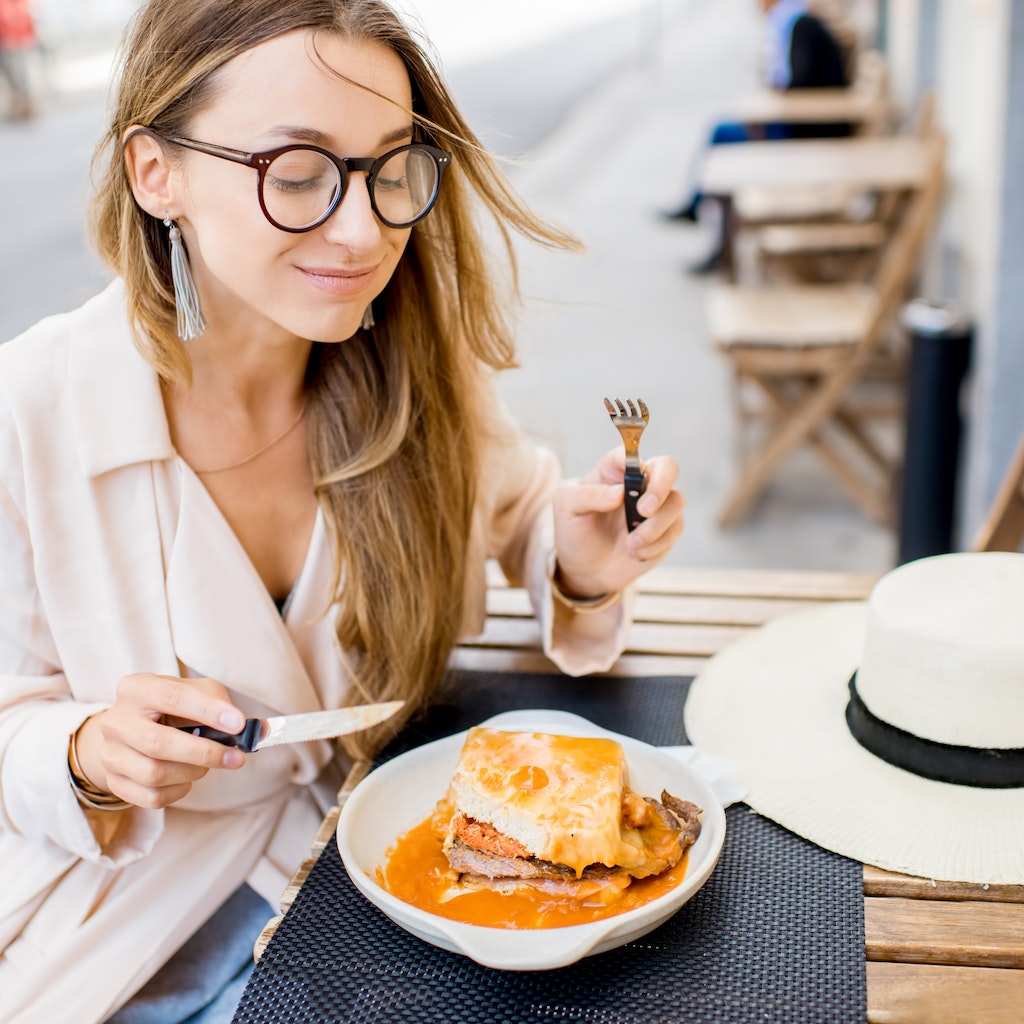 Woman eating traditional portuguese sandwich with meat called francesinha sitting at the restaurant in Porto city, Portugal
