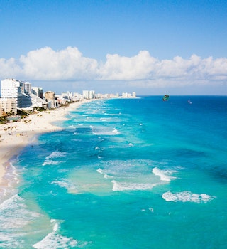 Aerial of Cancun beach on a sunny day with parasailers, swimmers and sunbathers. 